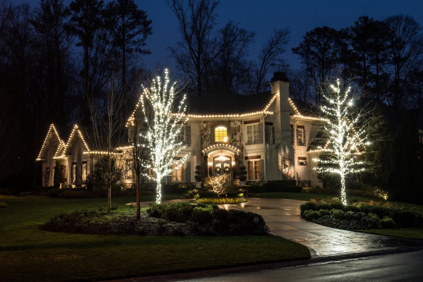 Roofline and tree lighting on a stone home at dusk