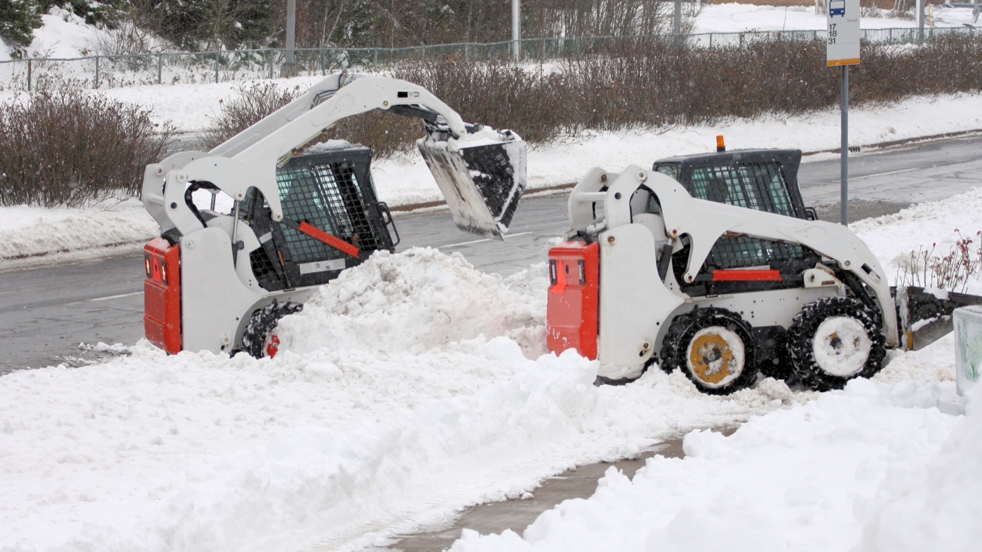 Skid steers clearing snow from a sidewalk